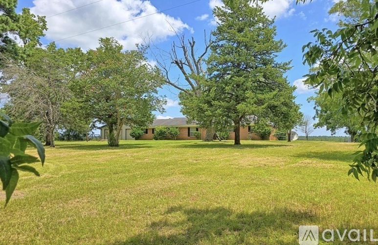 A grassy field with trees and a house in the background.