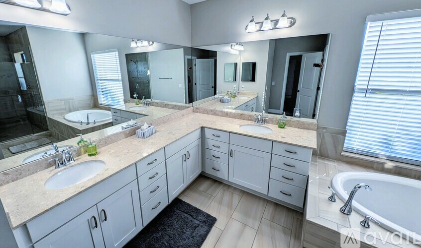 A modern bathroom with a large mirror, double sinks, and a bathtub.
