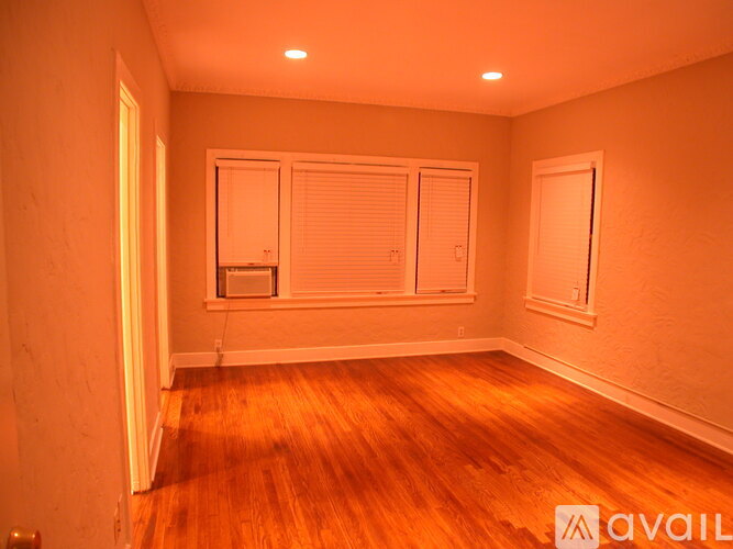 A room with wooden floors and white walls, with a window and a door.