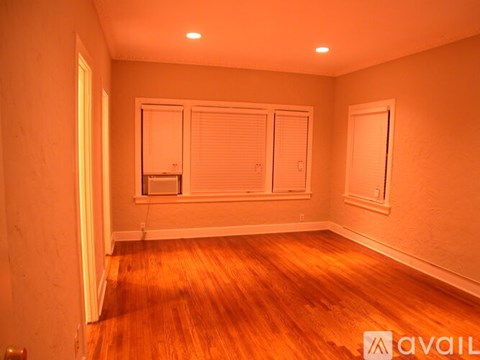 A room with wooden floors and white walls, with a window and a door.