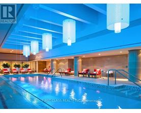 A swimming pool inside a building with red chairs around it.