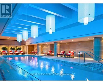 A swimming pool inside a building with red chairs around it.
