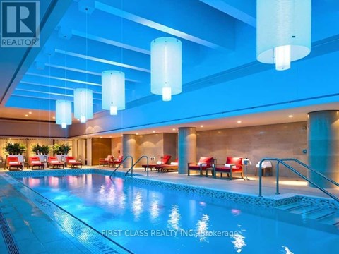 A swimming pool inside a building with red chairs around it.