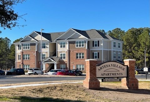 A large brick building with a sign that says "Artesa Village Apartments" in front of it.
