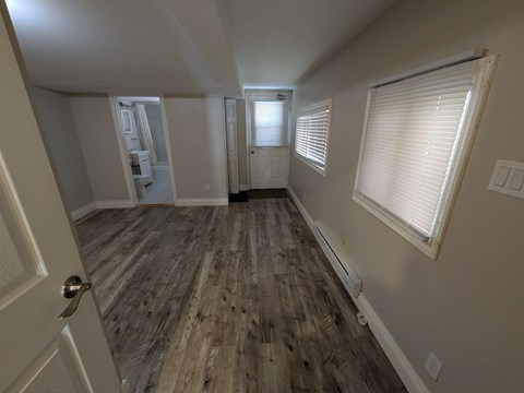 A room with wooden flooring and a door on the left side.