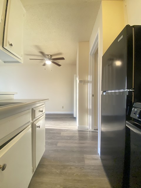 A black refrigerator is in a kitchen with white cabinets.