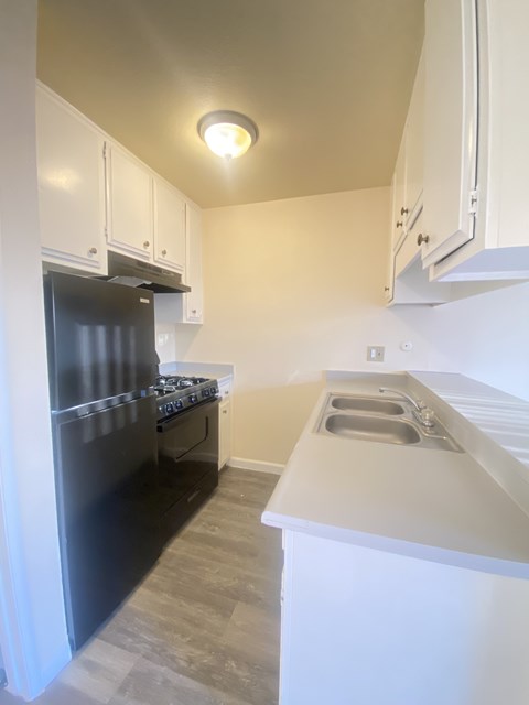 A kitchen with a black refrigerator and white cabinets.