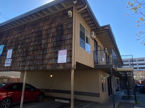A red car is parked in front of a building with a sign that reads 322.