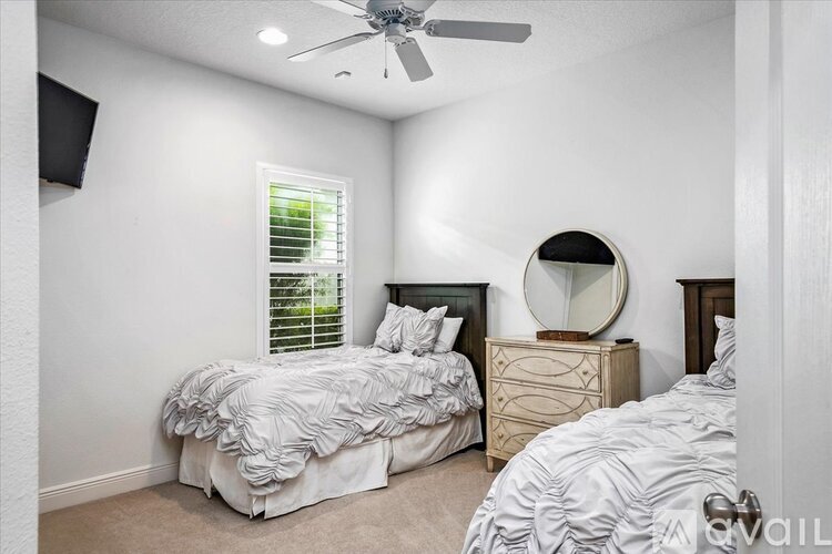 A bedroom with two beds, one with a white comforter and the other with a patterned comforter, a dresser with a mirror, and a ceiling fan.