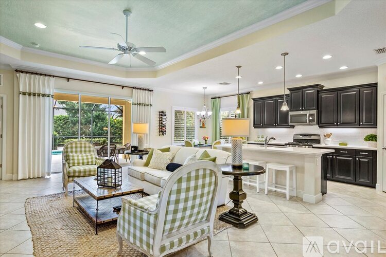 A living room with a green and white checkered chair and a kitchen area with black cabinets.