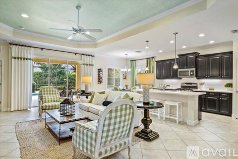 A living room with a green and white checkered chair and a kitchen area with black cabinets.