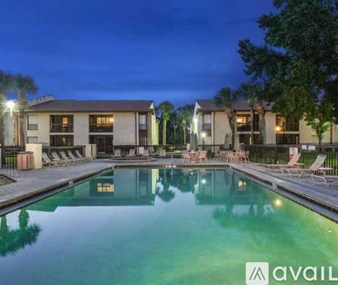 A pool area with lounge chairs and a building in the background at dusk.
