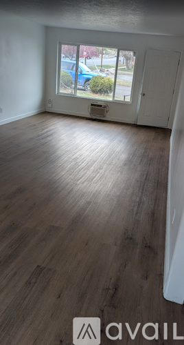 A room with wooden flooring and a window showing a blue car and trees outside.