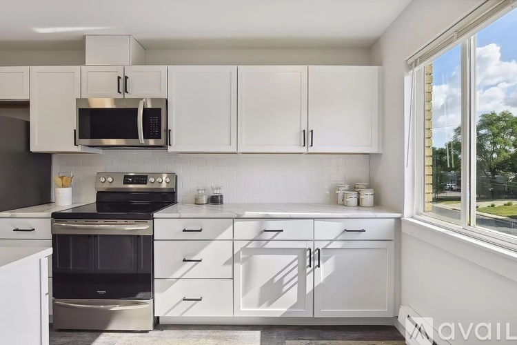 A kitchen with white cabinets and appliances, a window with a view of the outside, and a text "available" on the wall.