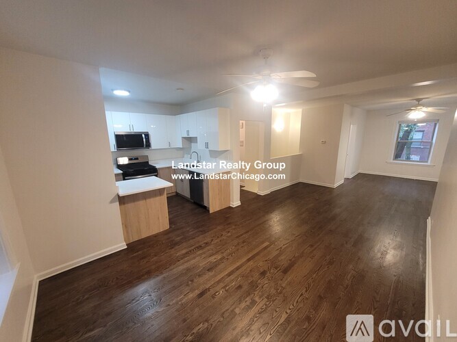 A spacious room with wooden flooring and white walls, featuring a kitchenette with a microwave and a refrigerator.
