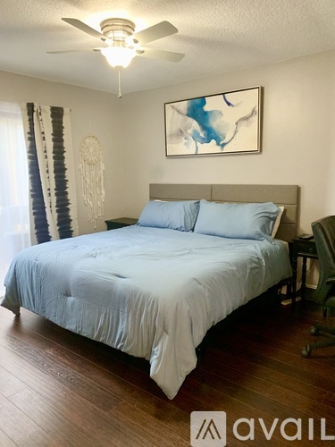 A bedroom with a bed, a ceiling fan, and a painting on the wall.