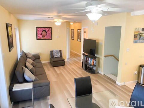 A living room with a grey couch, a black chair, a glass table and a television.