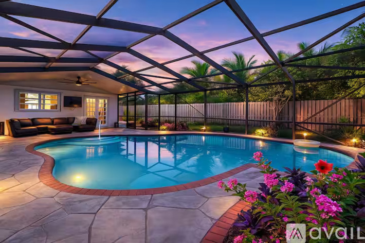 A pool surrounded by a fence and flowers with a house in the background.