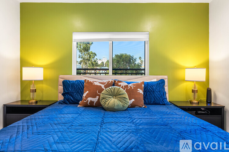 A bed with a blue comforter and a window showing a view of trees.