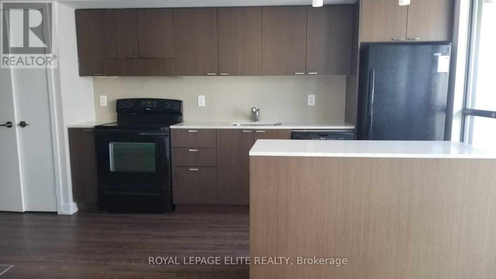 A kitchen with brown cabinets and a black fridge.