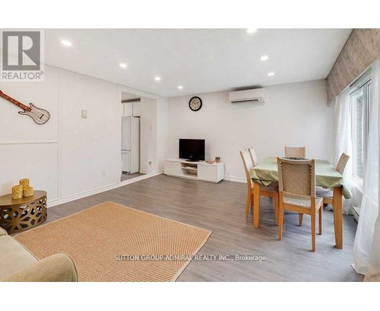 A living room with a brown rug, a wooden table with chairs, and a guitar hanging on the wall.