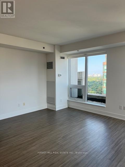 A spacious room with wooden flooring and a large window overlooking a cityscape.