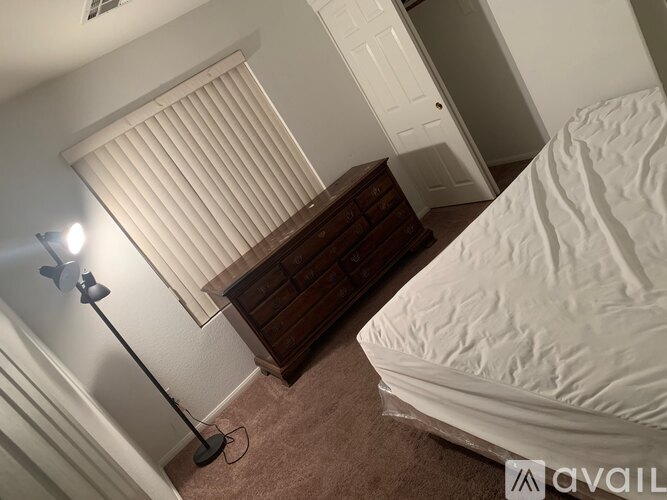 A bedroom with a bed, dresser, and window with blinds.