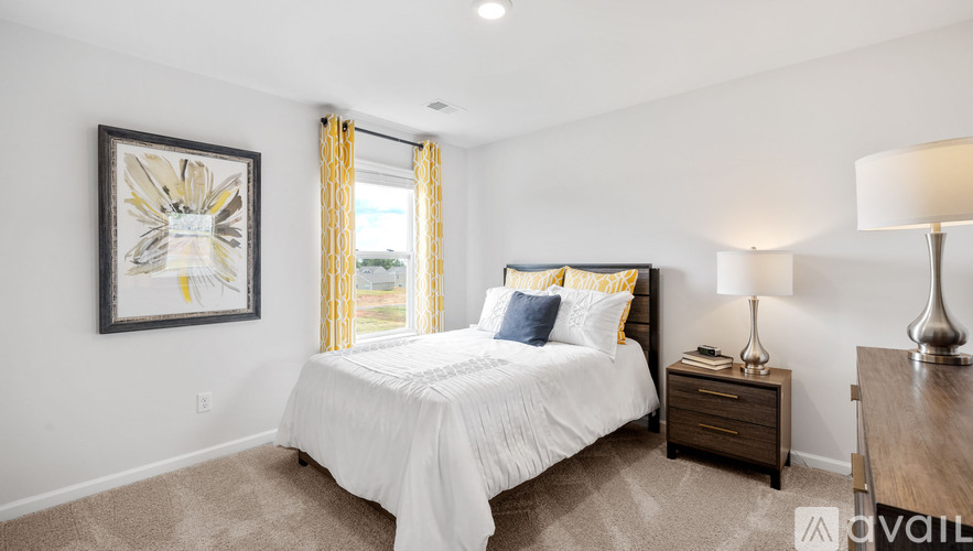 A bedroom with a large bed, a nightstand with a lamp, and a framed picture on the wall.