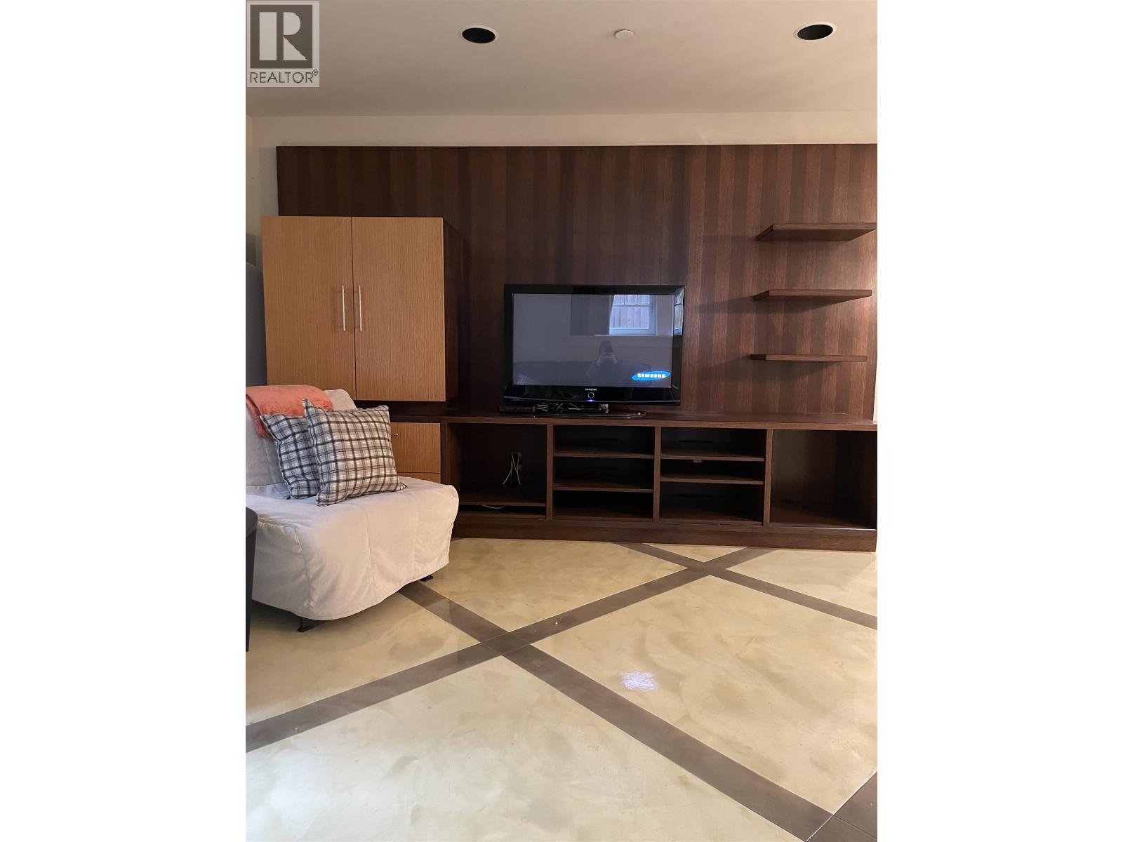 A living room with a couch, television, and wooden cabinets.