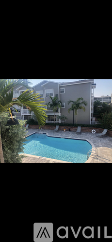A pool surrounded by a concrete patio and a building in the background.