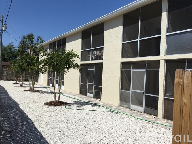 A building with a gravel lot in front and a tree in the corner.