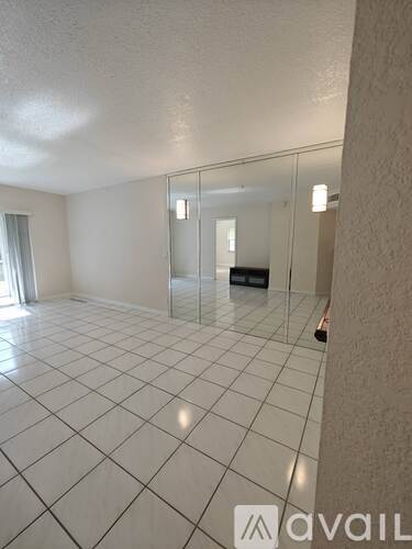 A spacious room with white tiled flooring and a glass door.
