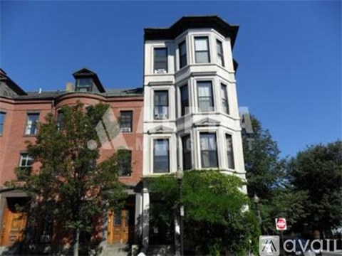 A tall white building with a black roof stands in front of a red brick building.