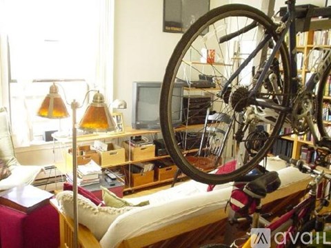 A bicycle wheel is hanging from the ceiling in a room with a desk and a chair.