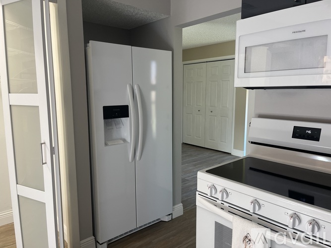A white refrigerator is in a kitchen with a stove and microwave.