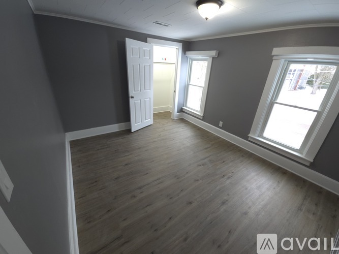 A room with grey walls and wooden flooring, featuring a white door and windows.