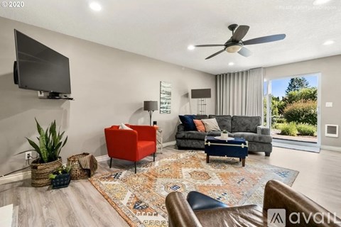 A living room with a grey couch, a red chair, a black chair, a rug, a television, and a ceiling fan.