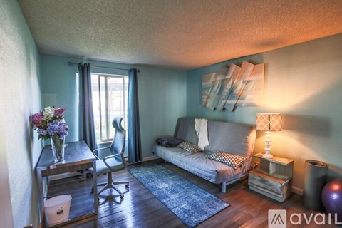 A living room with a grey couch, a wooden table, a chair, a window with curtains, and a painting on the wall.