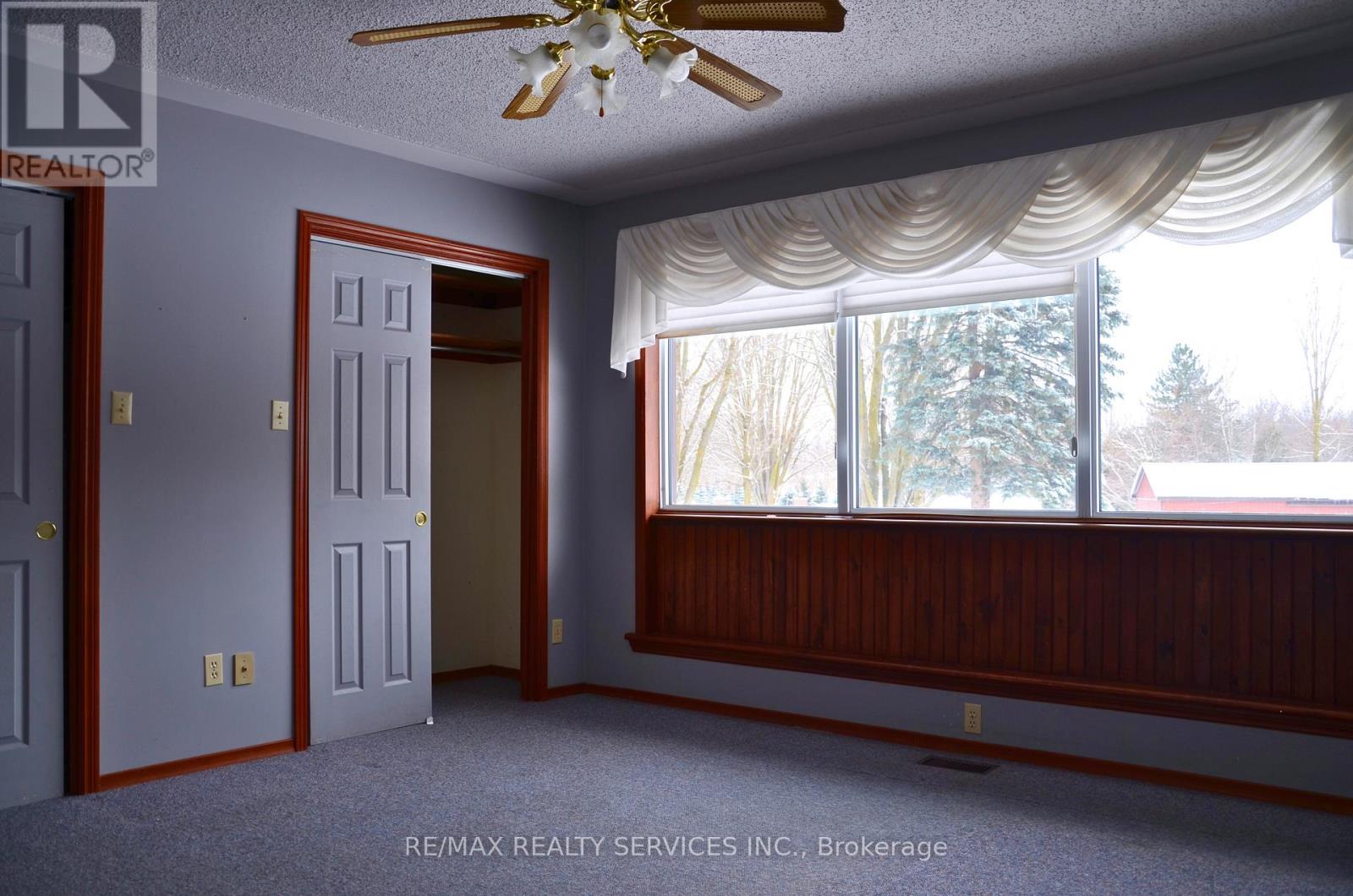 A room with a ceiling fan and a window with a view of trees.