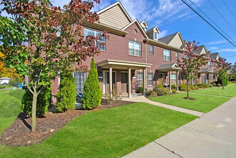 A row of houses with green lawns and trees in front.
