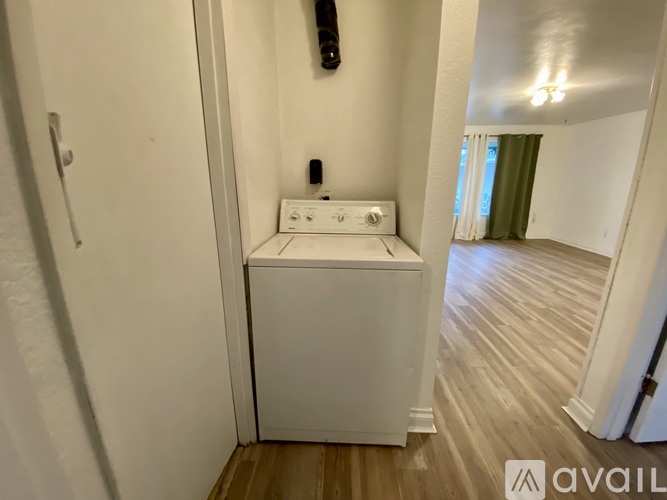 A small white washing machine is in a narrow room.