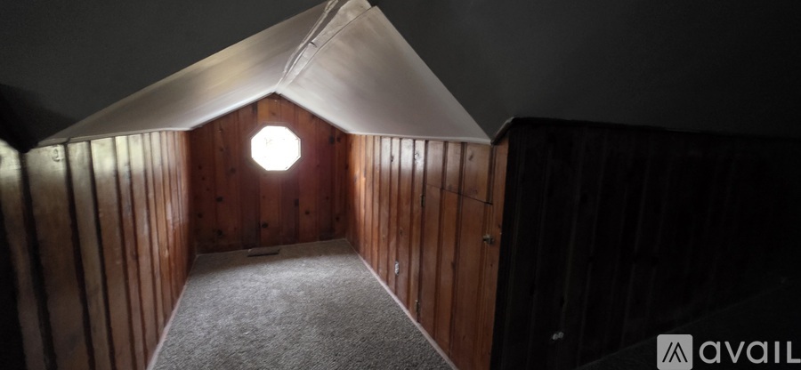 A wooden room with a carpeted floor and a round window.