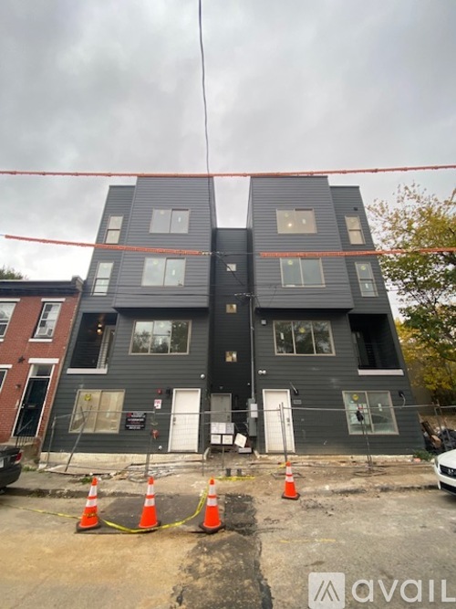 A grey two-story building with a red line in the middle and orange cones in front.