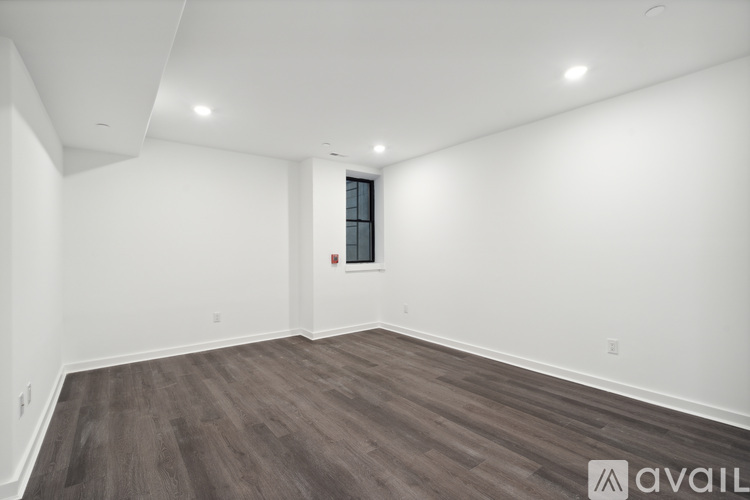 A spacious room with wooden flooring and a window with a red frame.