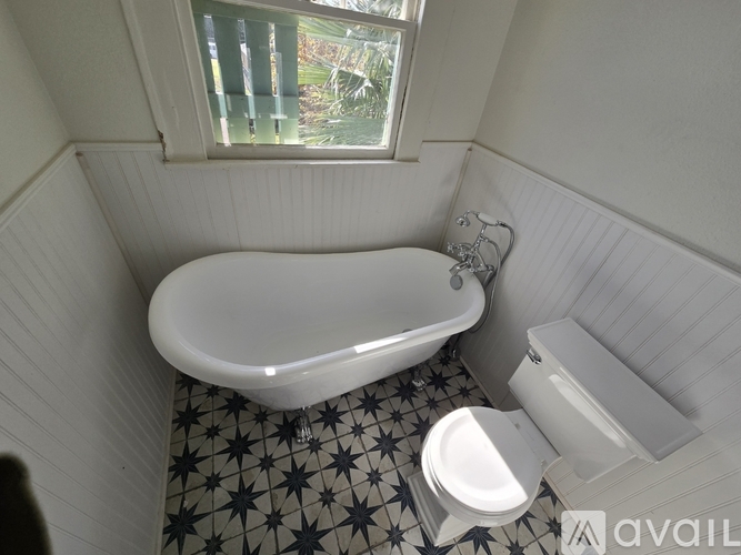 A white bathtub with a star patterned floor and a toilet next to it.
