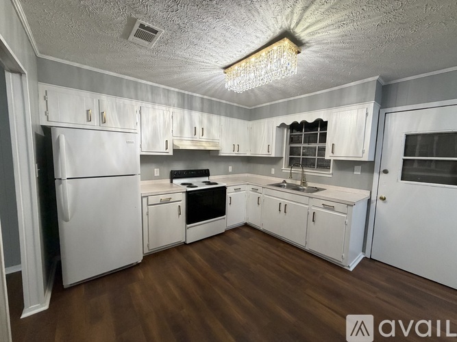 A kitchen with white cabinets and appliances, a wooden floor, and a chandelier hanging from the ceiling.