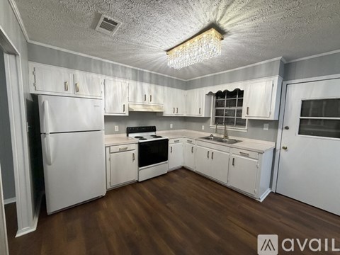 A kitchen with white cabinets and appliances, a wooden floor, and a chandelier hanging from the ceiling.