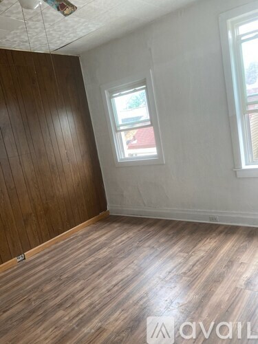A room with wooden floors and a window showing a red building outside.