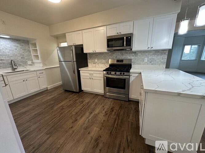 A kitchen with a black refrigerator, white cabinets, and a wooden floor.