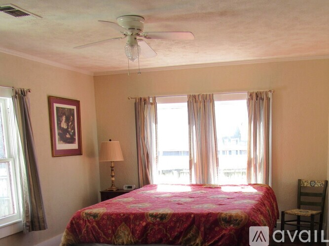 A bedroom with a bed, a ceiling fan, and a window with curtains.